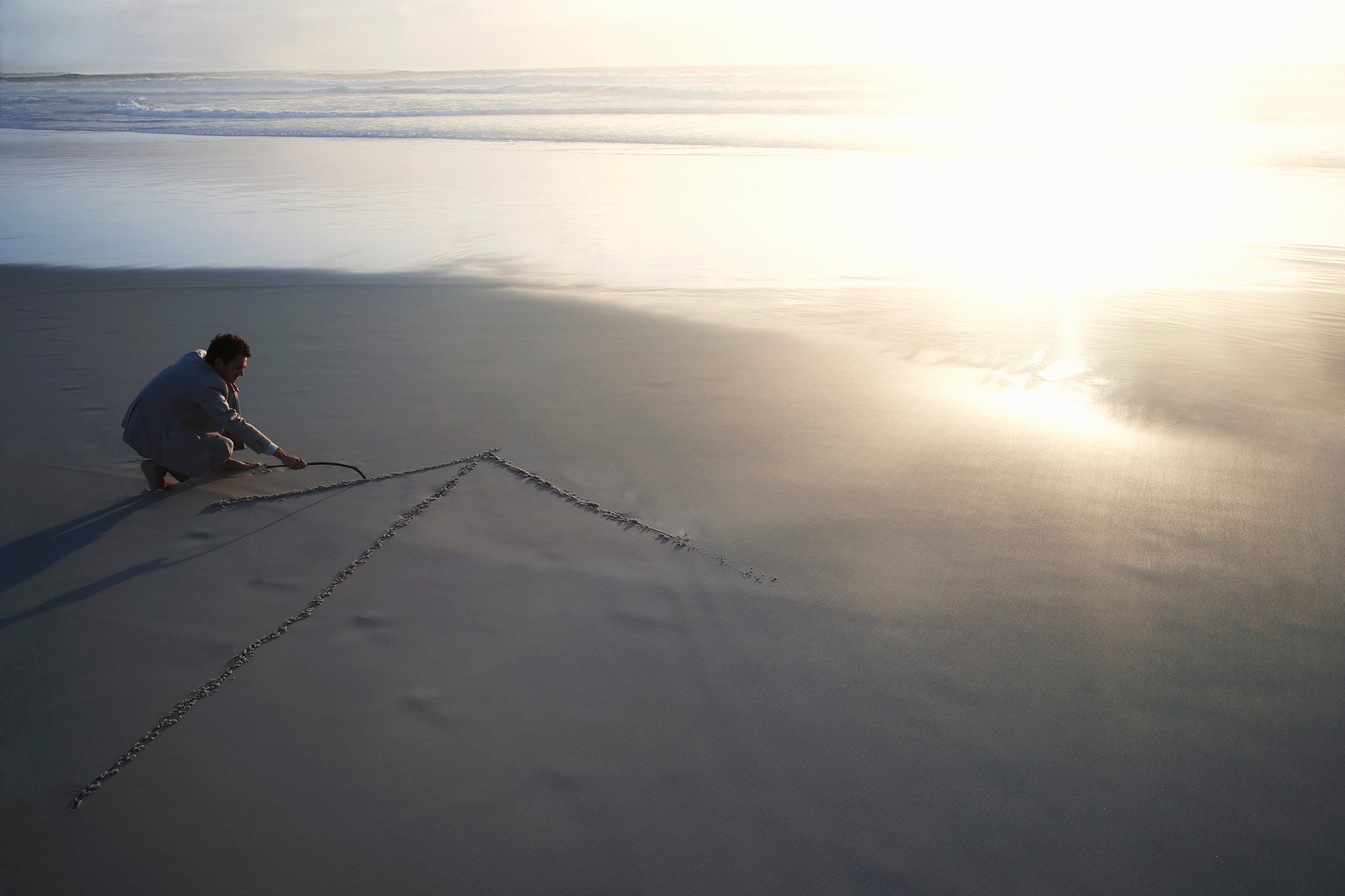 Business man drawing arrow in sand on beach elevated view