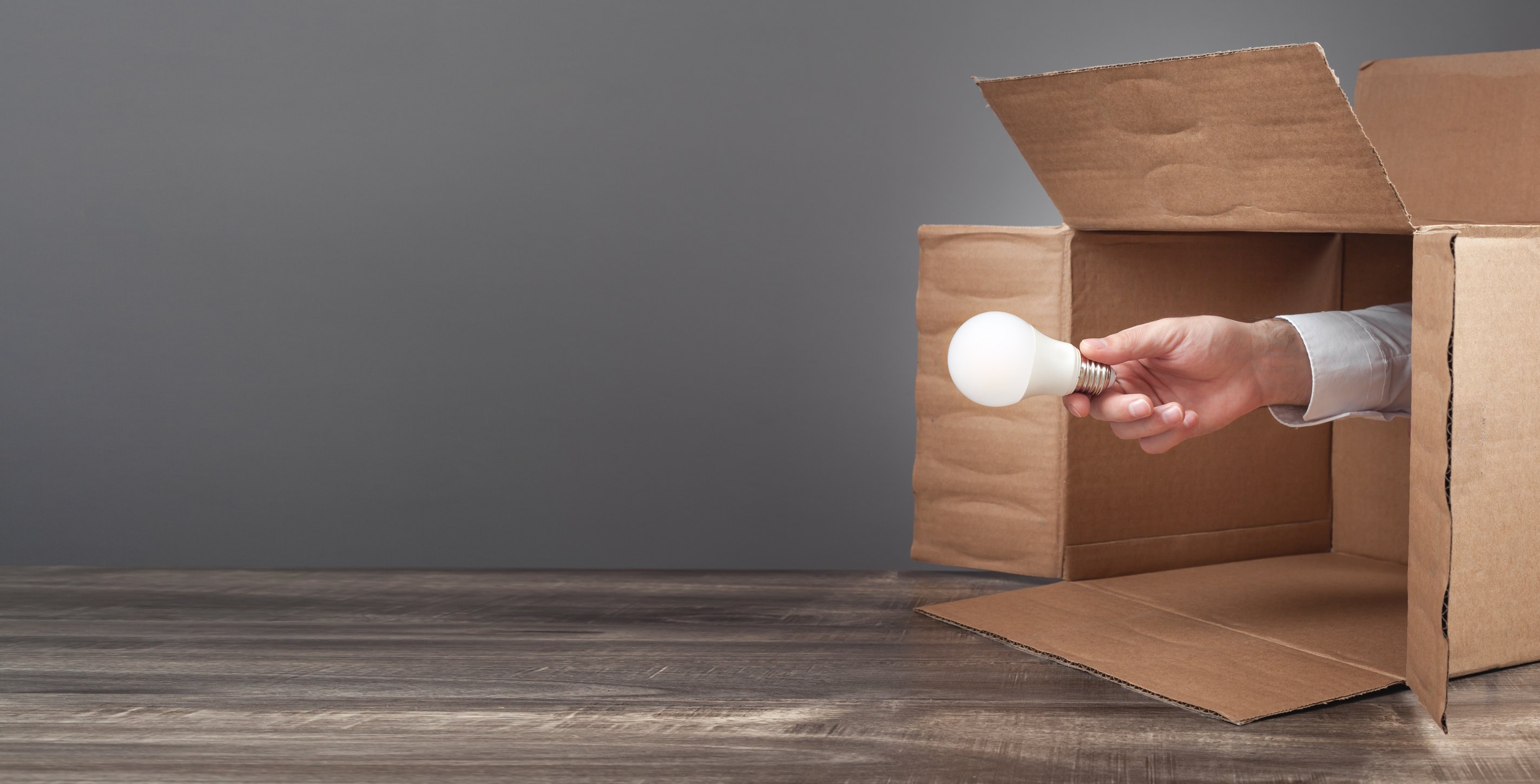 Male hand holding a light bulb coming out from a cardboard box. Think Out Of The Box